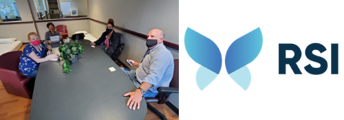 “Four people sit distanced around a conference table during a meeting, each wearing face masks. A potted plant sits in the center of the table. Next to the meeting photo is the RSI logo featuring two overlapping blue butterfly-shaped wings and the letters ‘RSI.