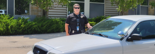 Co Responder officer standing beside gray officer car outside of the Crisis center.