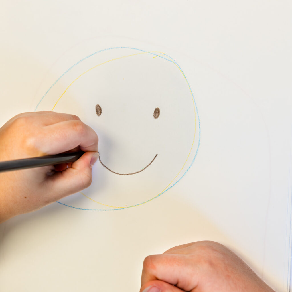 Child drawing a smiley face with colored pencil.