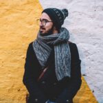 Man dressed in winter clothes looking off into the distance standing against a wall.