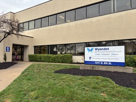 Exterior photo of Downtown Wellness Center with monument sign displaying logos of Wyandot Center, PACES, Kim Wilson Housing and the University of Kansas Health System