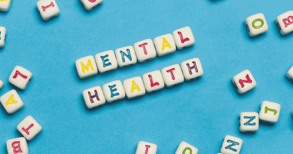 Colorful letter tiles spelling "Mental Health" on a blue background, representing mental wellness and emotional well-being.